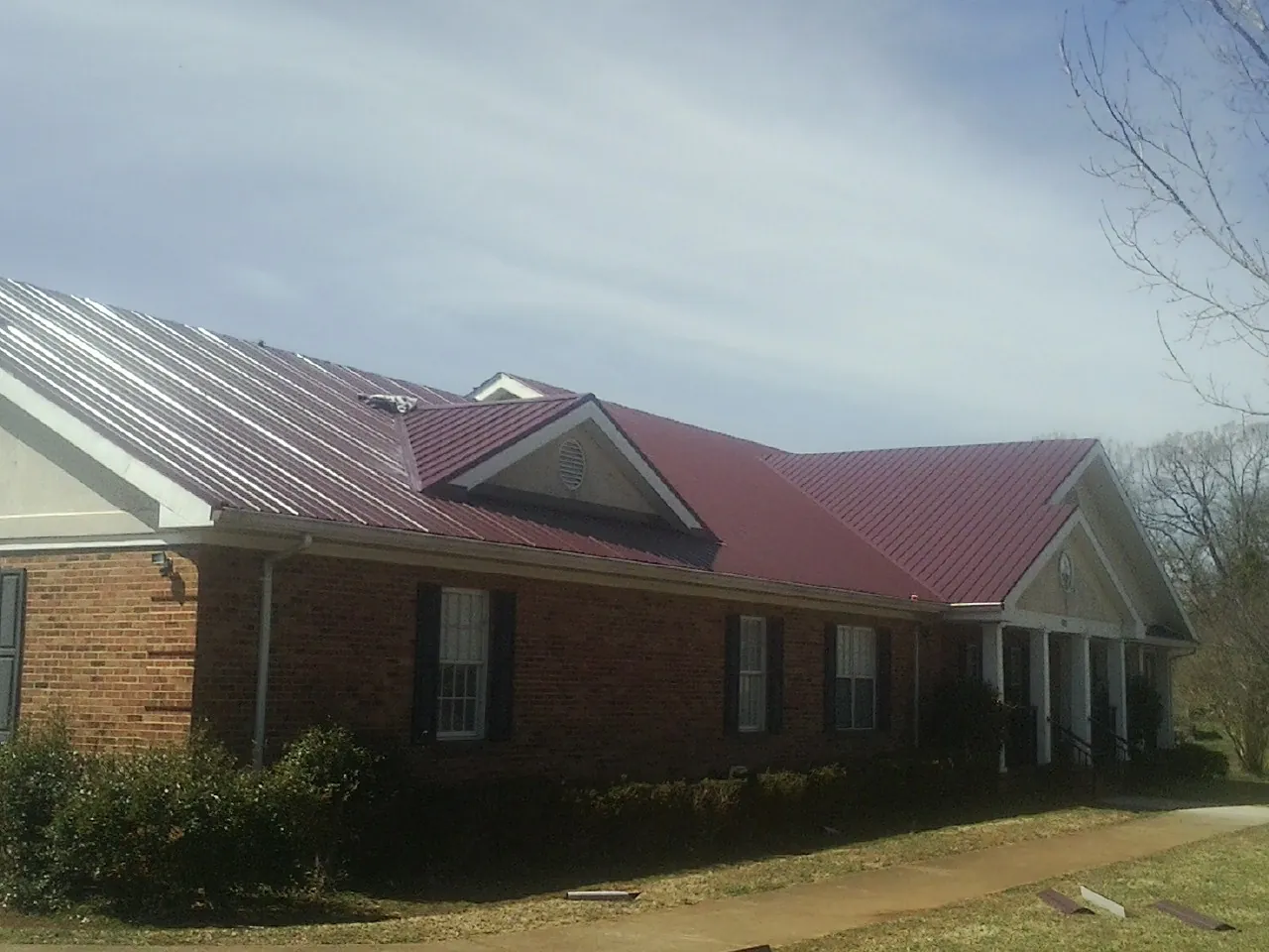 Red metal roof with gabled entries on a long brick building, from a Hail Damage Roof Repair job in Russellville