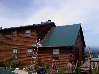 Green metal roof going on a two story log home with ladders set in Russellville