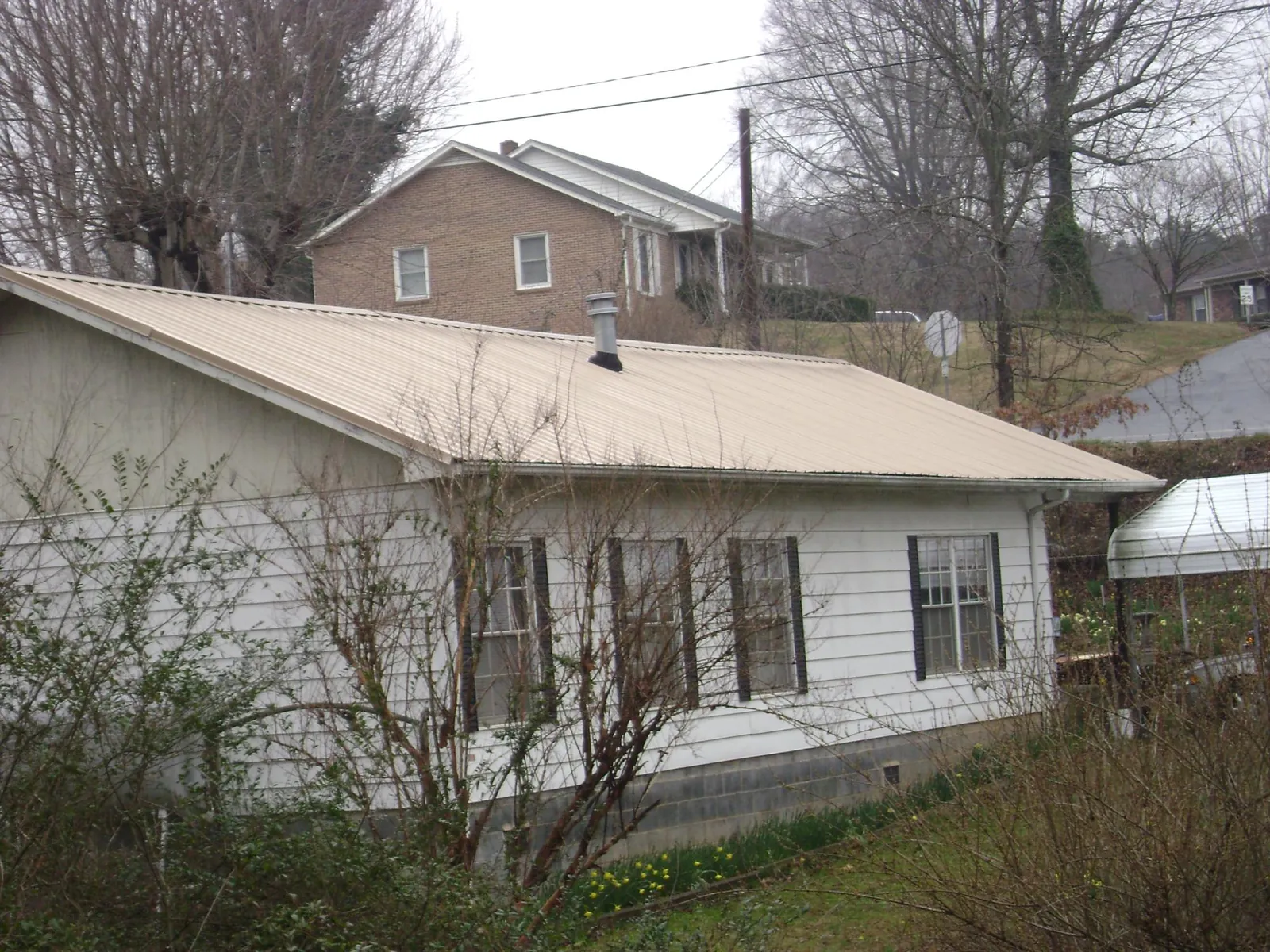 Tan metal roof on a white sided house set into a hillside — Commercial Roofing by Roofing Brothers in Russellville